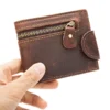 Hand holding a brown leather zip wallet with snap closure