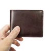 Hand holding a dark brown leather bifold wallet, studio shot