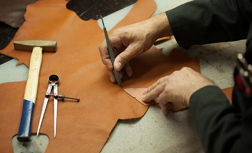 Factory craftsman cutting genuine cowhide leather for custom leather bags
