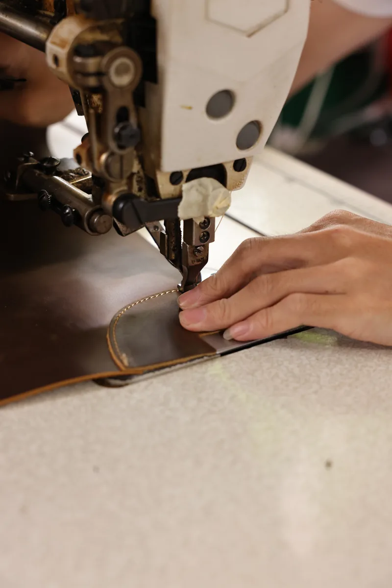 Hands stitching a curved leather component on an industrial sewing machine