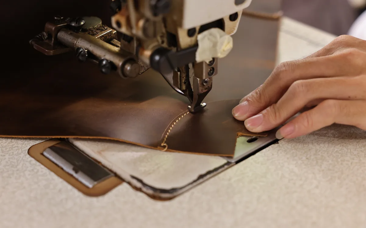 Close-up of a leather panel being stitched on an industrial sewing machine