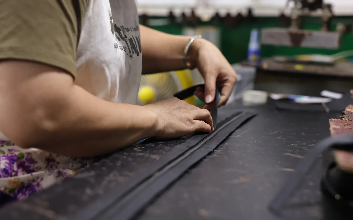 Hands aligning a narrow black trim strip on a leather bag panel