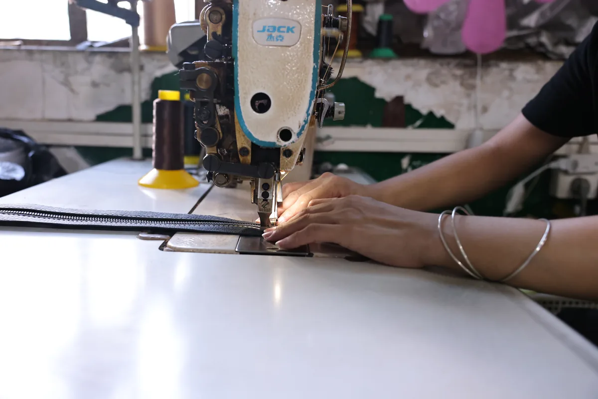 Hands guiding a leather bag panel through an industrial sewing machine