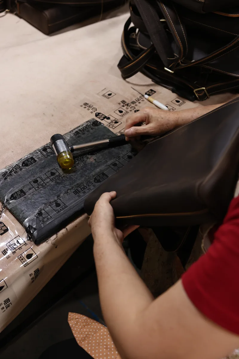 Worker positioning a metal fitting on a brown leather bag panel