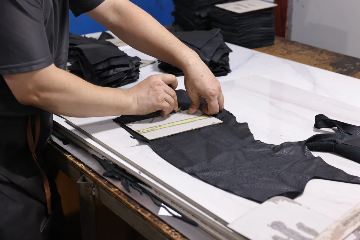 Hands positioning a paper template on dark leather bag panels