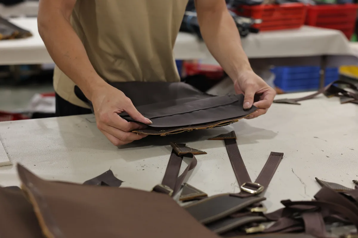 Hands aligning leather panels and straps during bag assembly