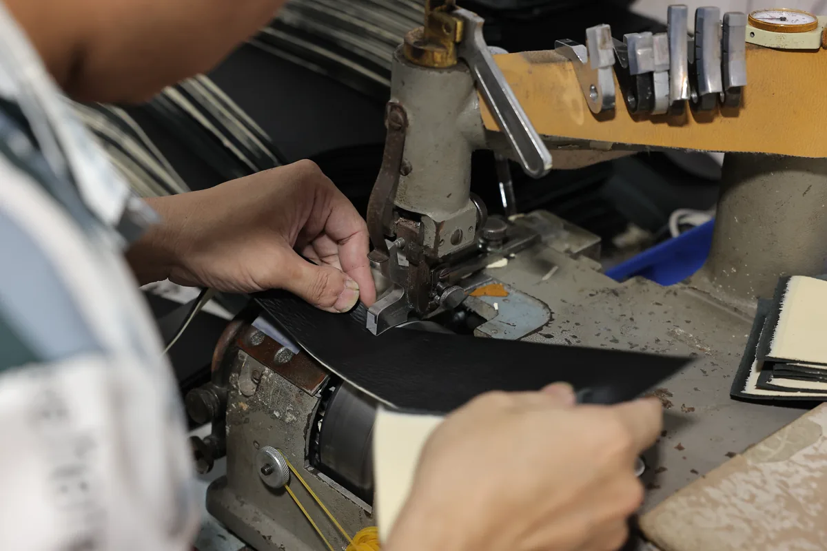 Hands guiding a leather bag panel through an edge-working machine