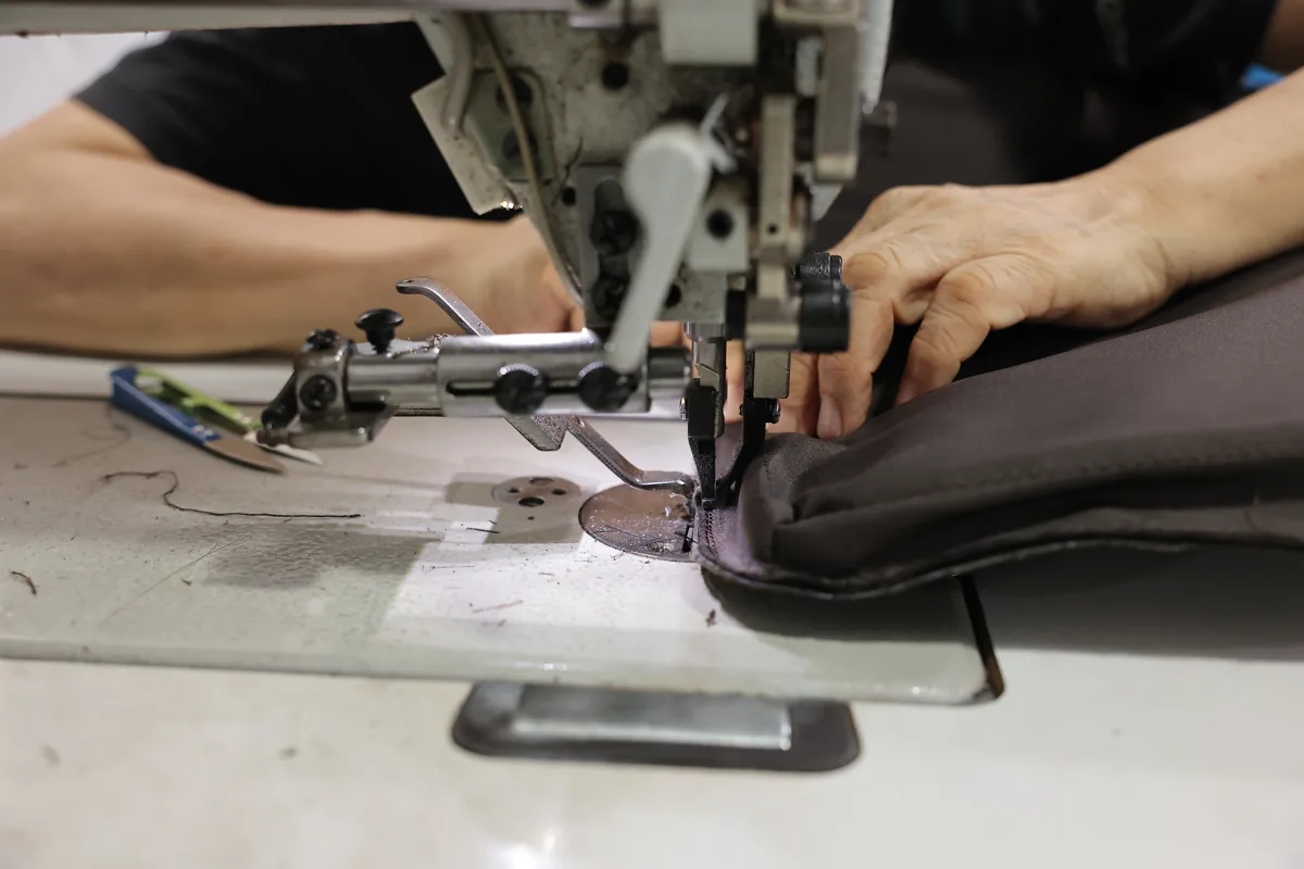 Hands sewing the edge of a leather bag body on an industrial machine