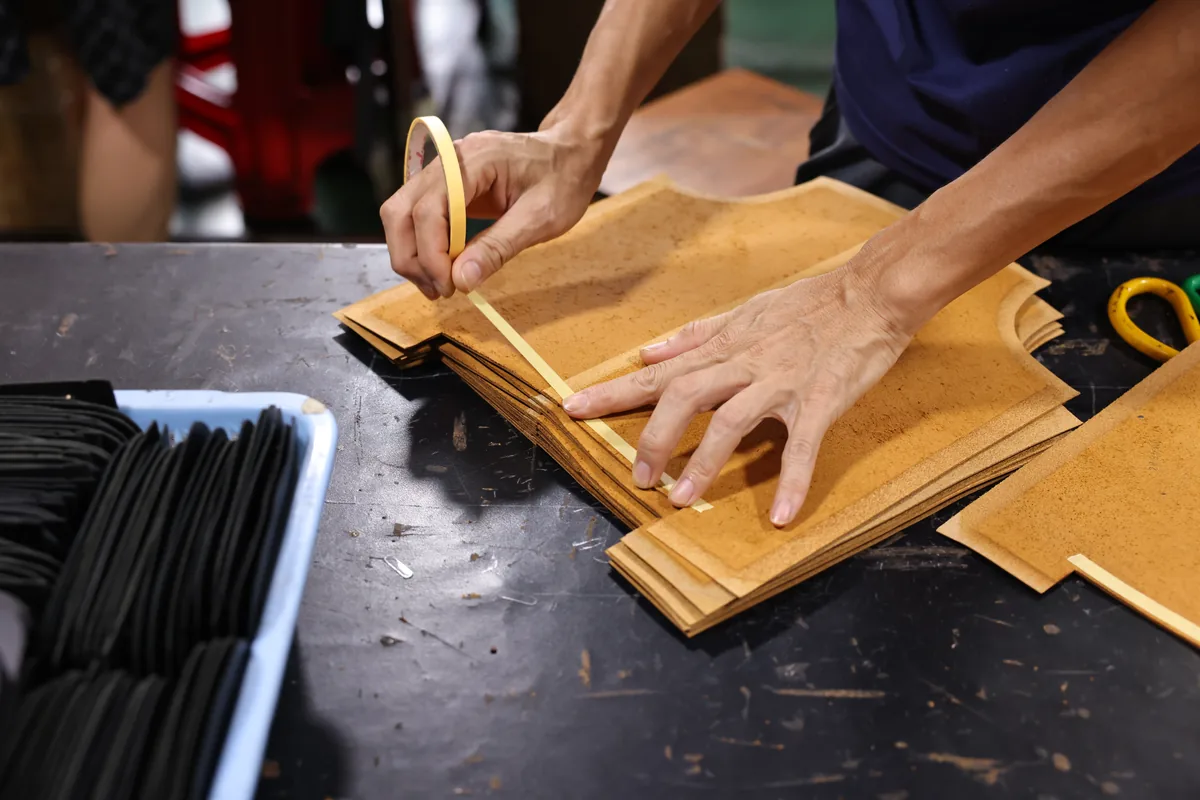 Hands marking a batch of tan leather bag panels before assembly