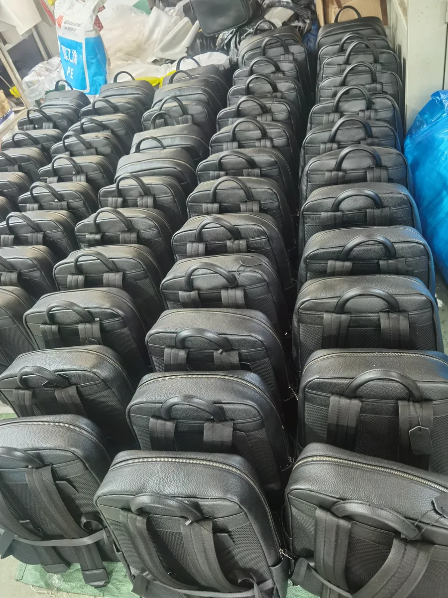 Rows of black backpacks with webbing handles in a factory storage area