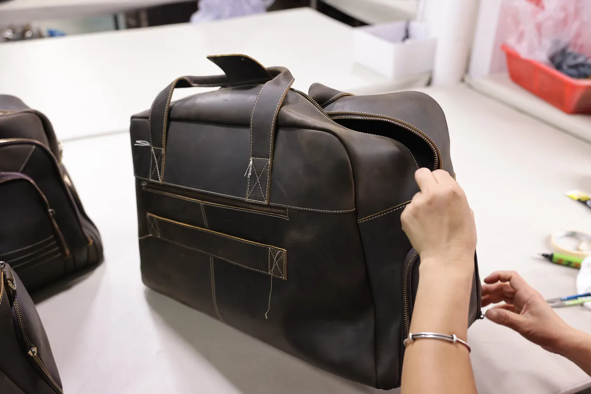 Hands working on the zipper and body of a leather bag in the factory