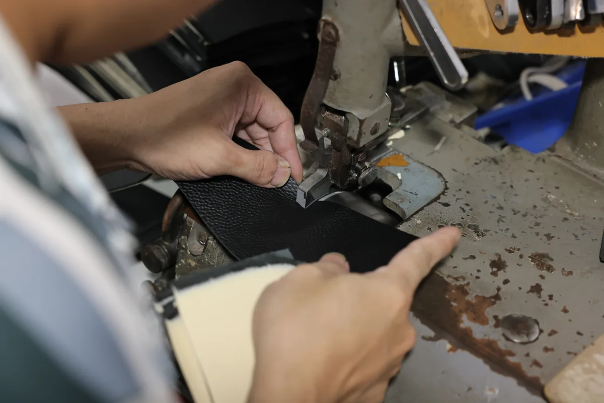 Hands guiding a black leather panel through a factory machine