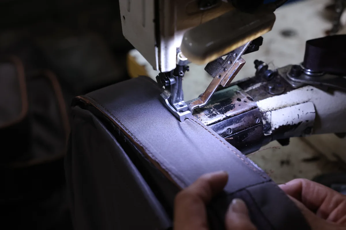 Hands guiding a black leather bag panel through a sewing machine