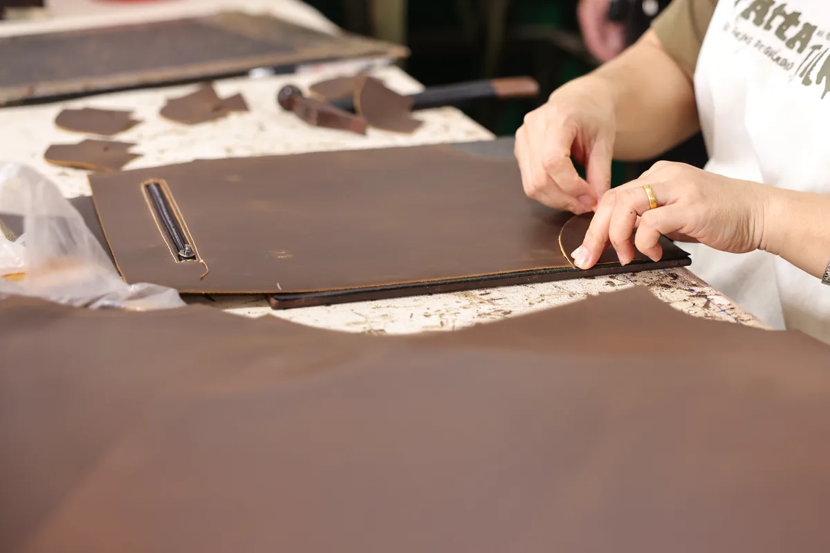 Worker checking brown leather bag panels at a production table
