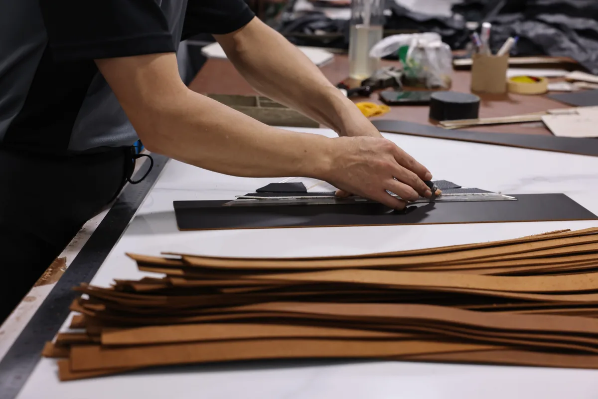 Worker aligning long brown leather bag panels beside a cutting template