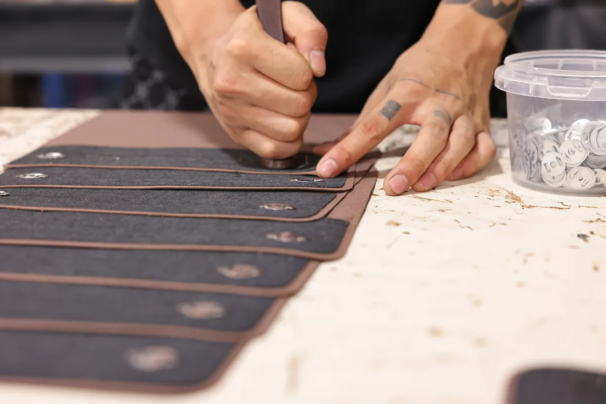 Hands marking narrow brown leather bag panels before assembly