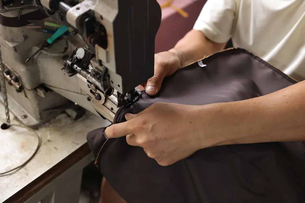 Hands guiding a leather bag panel through an industrial sewing machine
