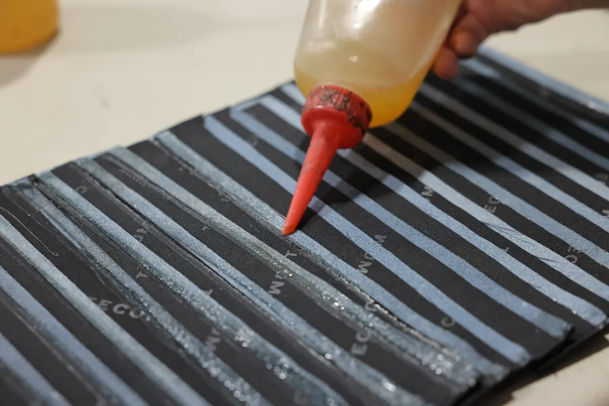 Adhesive being applied to a striped leather component at a factory workbench