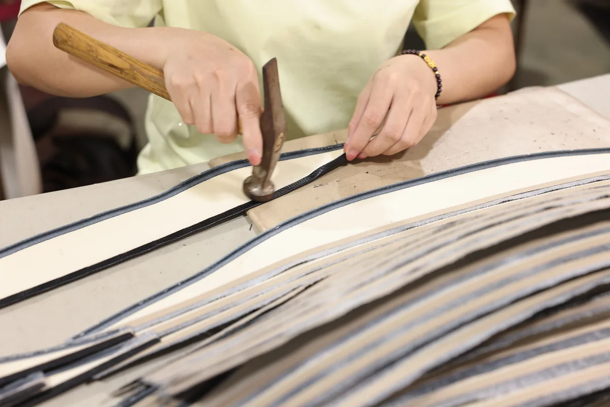 Hands cutting layered material for leather bag production