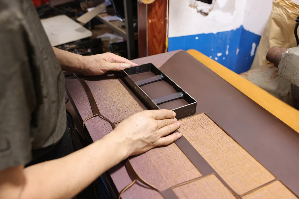 Hands arranging layered leather bag panels during assembly