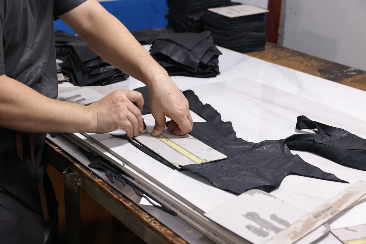 Hands arranging a paper pattern over dark leather bag panels
