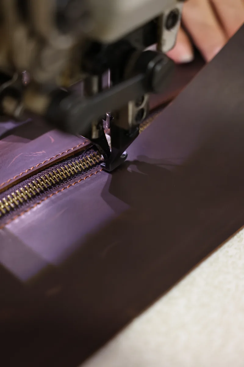 Close view of a zipper seam being sewn into a leather bag panel