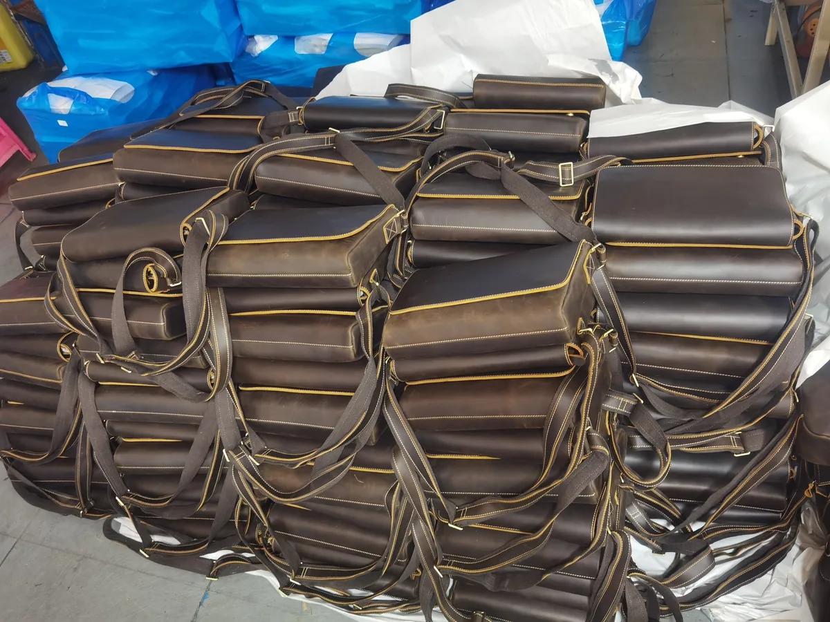 Brown leather shoulder bags with contrast stitching stacked in a workshop