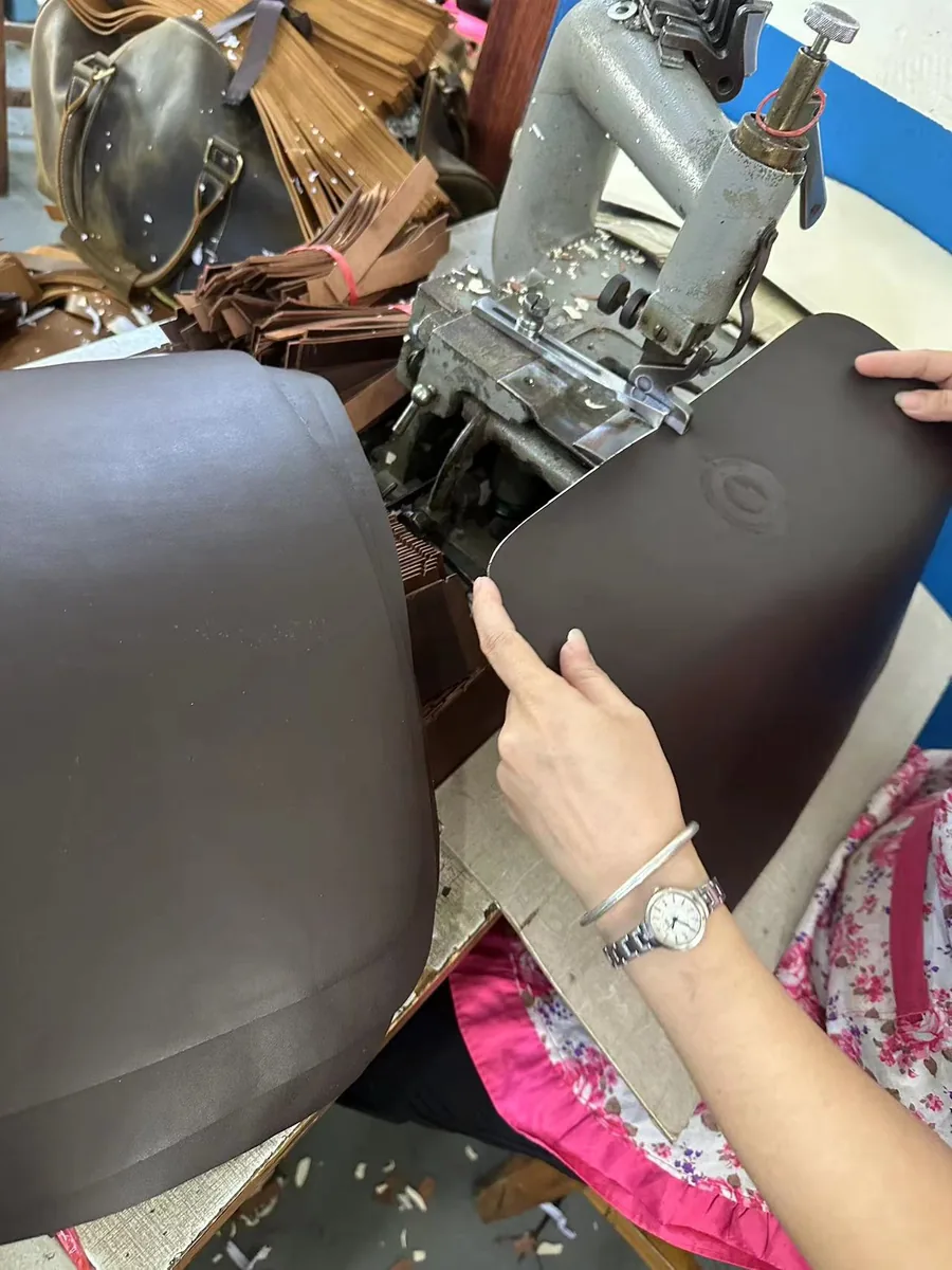 Worker guiding a leather bag panel through an industrial sewing machine